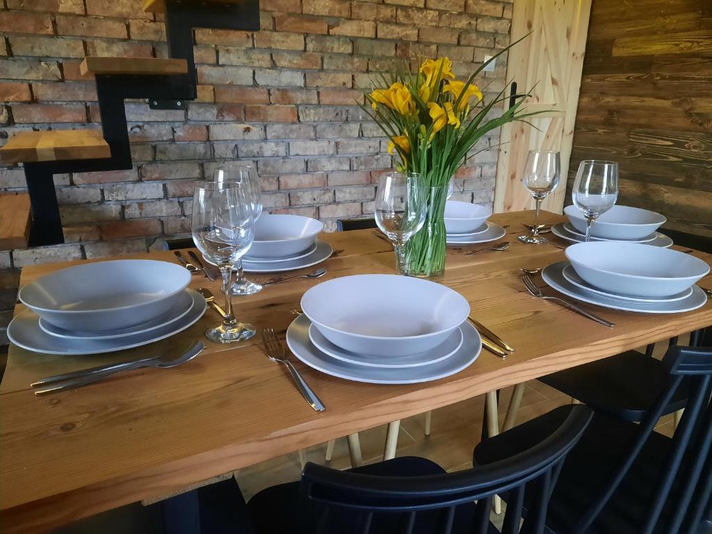 una mesa de madera con platos y vasos y un jarrón de flores en Mazurska Łąka, en Piecki