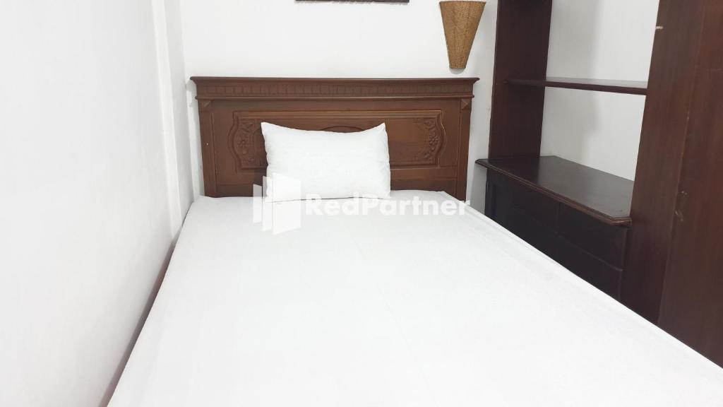un letto bianco con testiera in legno e cuscino bianco di Castle Residence Syariah RedPartner a Siwalapkerto