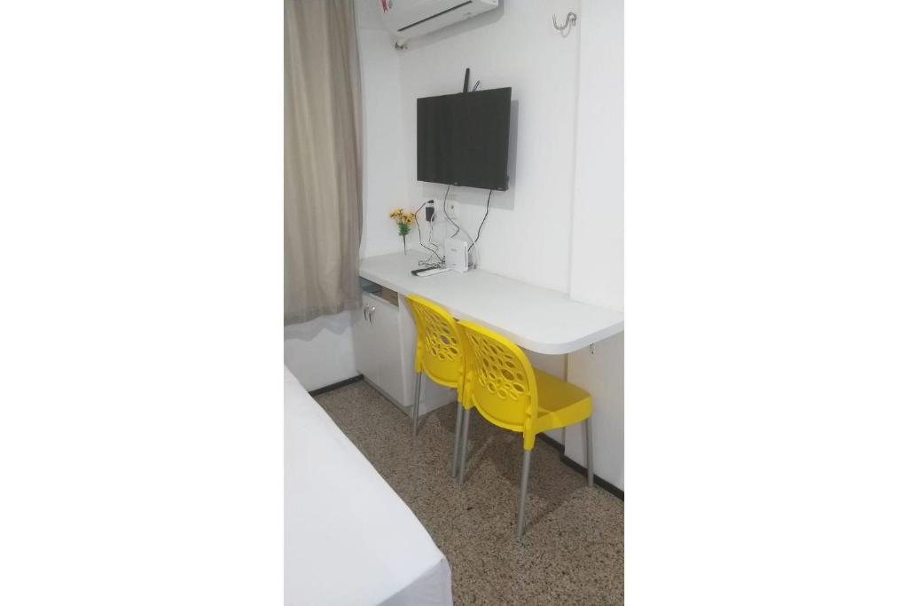 Cette chambre dispose d'un bureau, d'une télévision et de chaises jaunes. dans l'établissement 104 Apart mobiliado vista mar Praia de Iracema, à Fortaleza