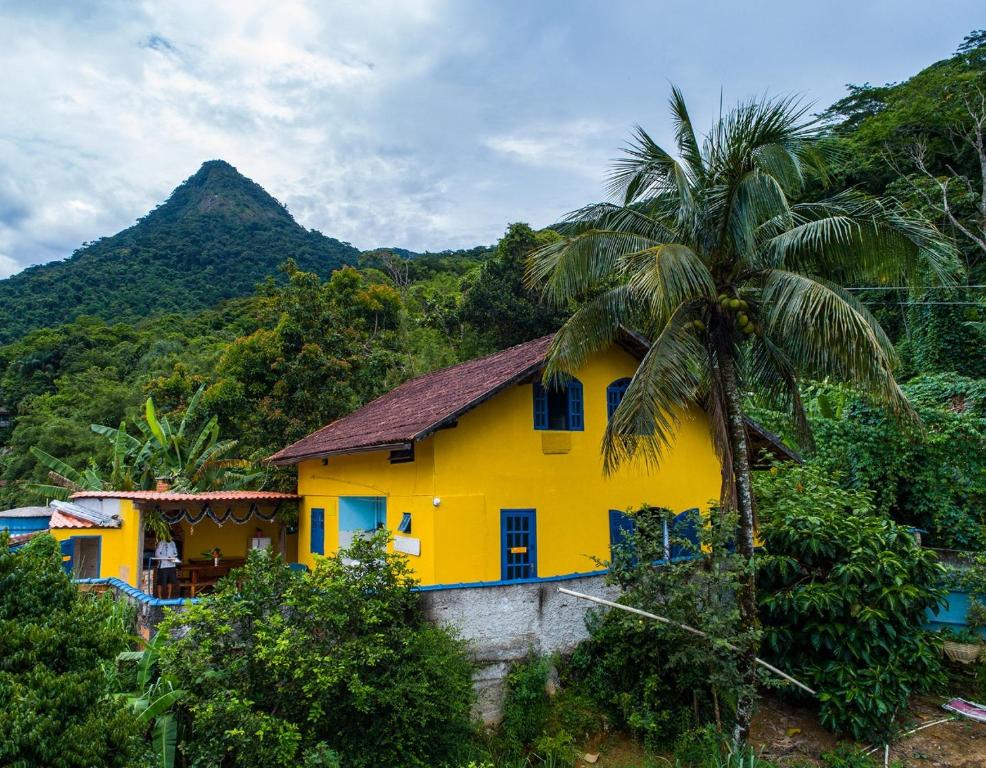 a yellow house with a palm tree in front of a mountain at Casa dos Franceses Ilha Grande in Abraão