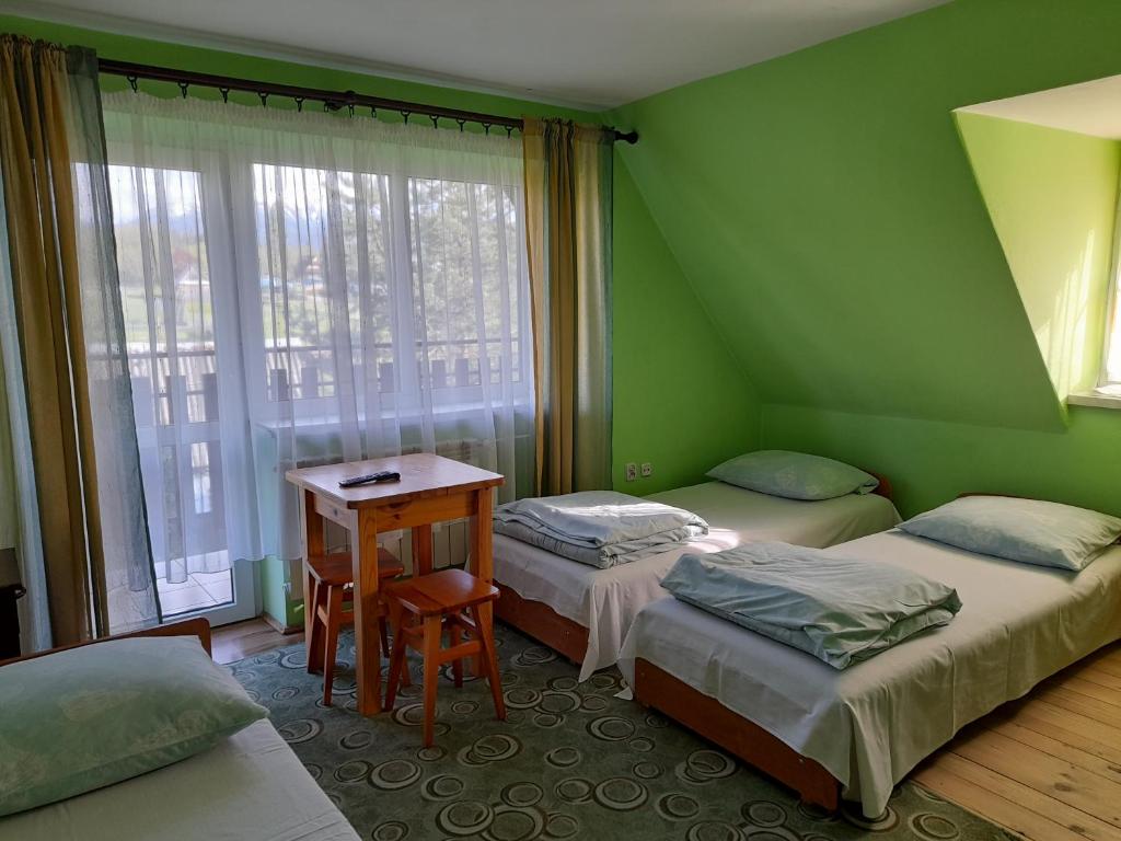 ポロニンにあるNad Potokiemのベッド2台、テーブル、窓が備わる客室です。