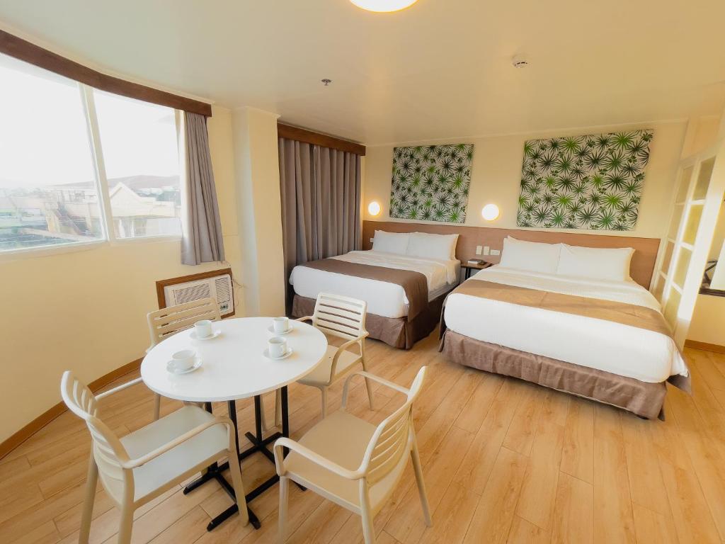 レガスピにあるHotel Sentro Legazpiのベッド2台、テーブルと椅子が備わるホテルルームです。