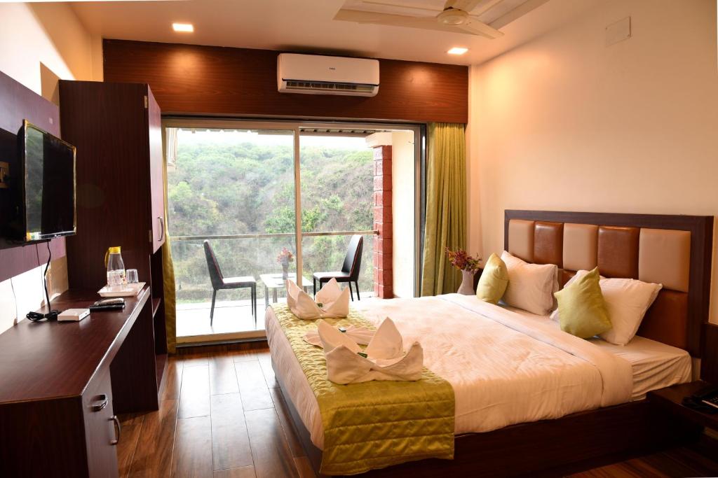 a bedroom with a bed with a desk and a large window at Khushi Riverside Resort & Spa in Mahabaleshwar