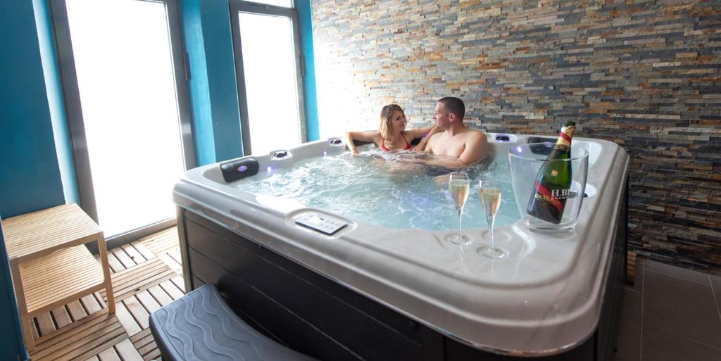 a man and woman in a hot tub with a bottle of champagne at Les Suites Fénelon in Le Cateau