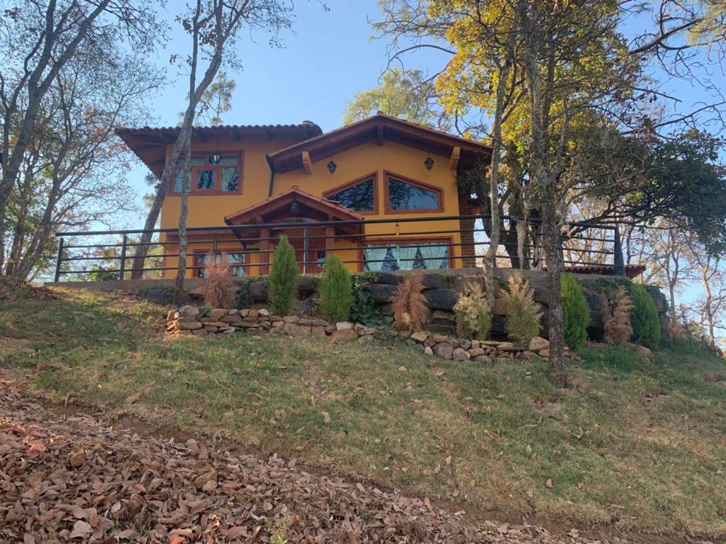 uma grande casa amarela numa colina na floresta em Cabaña Verito em Mazamitla