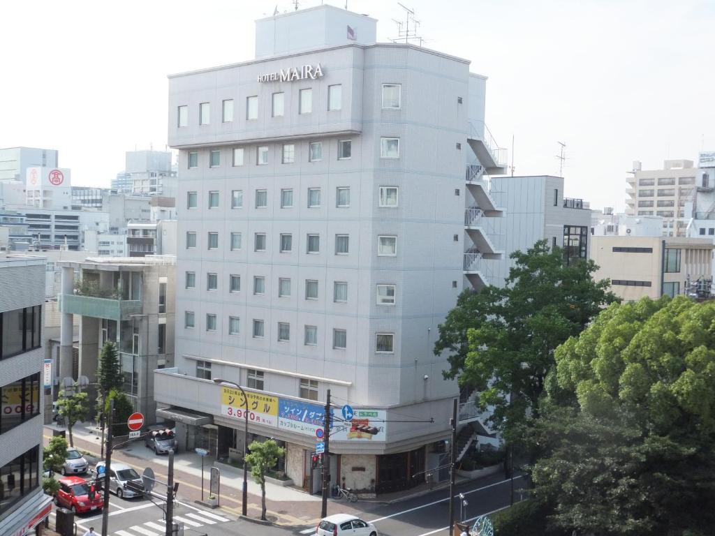 ein hohes weißes Gebäude in einer Stadtstraße mit Autos in der Unterkunft Hotel Maira in Okayama