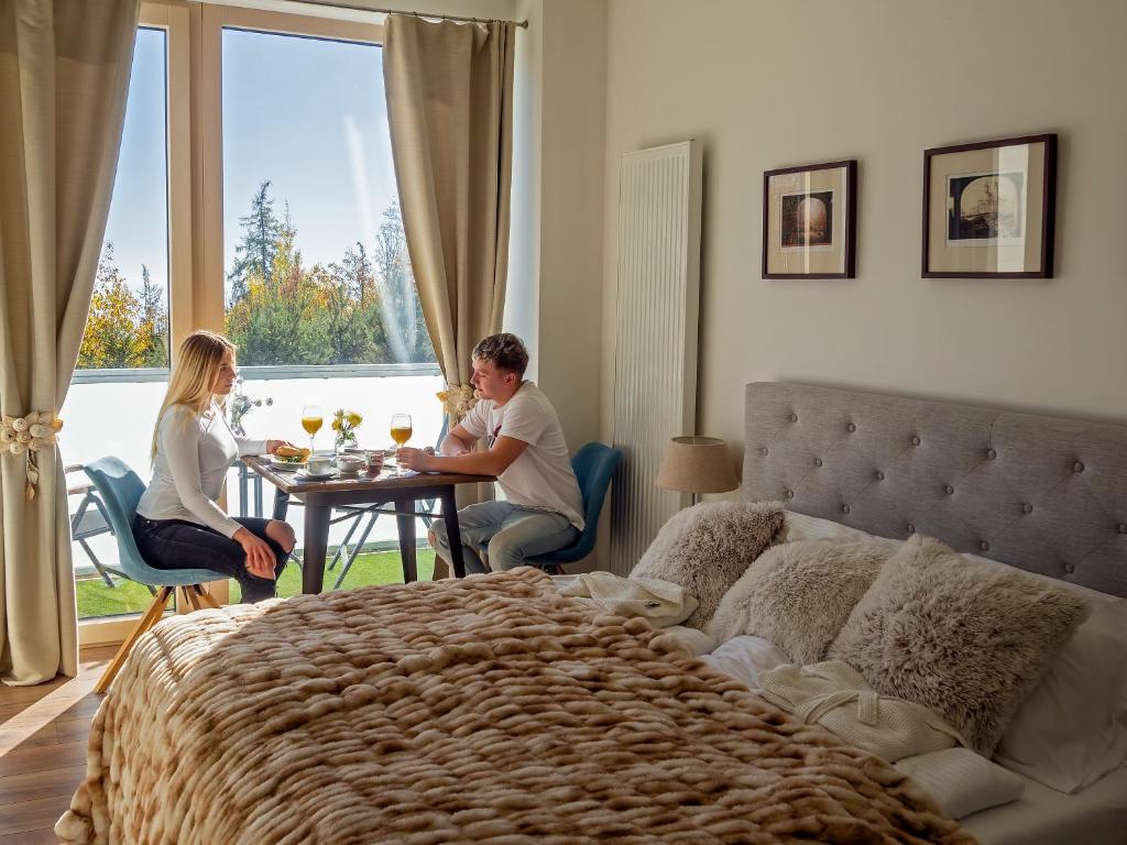 two people sitting at a table in a bedroom with a bed at Cozy Studio with NETFLIX - Apartmanovy dom Bernard in Nový Smokovec