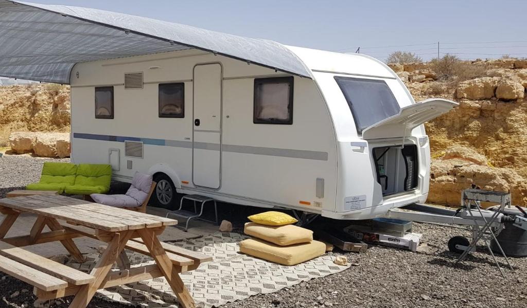 a white camper parked next to a picnic table at Itav Bateva Caravans - ייטב בטבע קרוואנים in Mitzpe Ramon