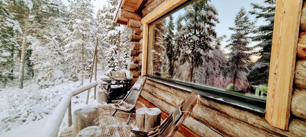 ein Fenster einer Hütte mit einem schneebedeckten Wald in der Unterkunft Cozy Log Cabin by Invisible Forest Lodge in Rovaniemi