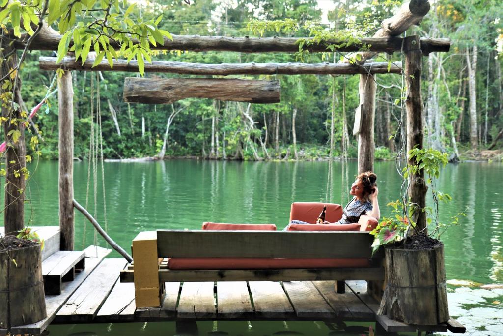 a woman sitting on a bench on a dock near a lake at El Hotelito Perdido in Rio Dulce