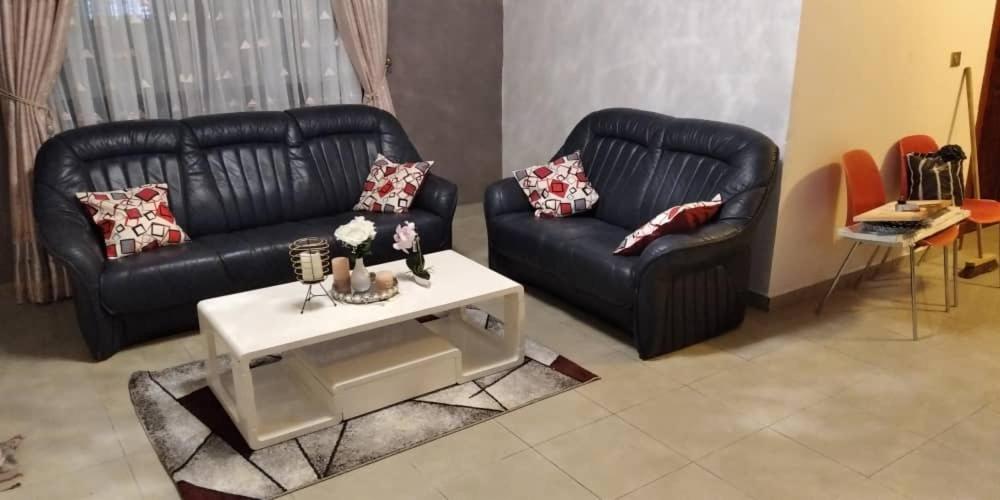 a living room with two black leather couches and a table at Appartements meublés Sorel in Douala