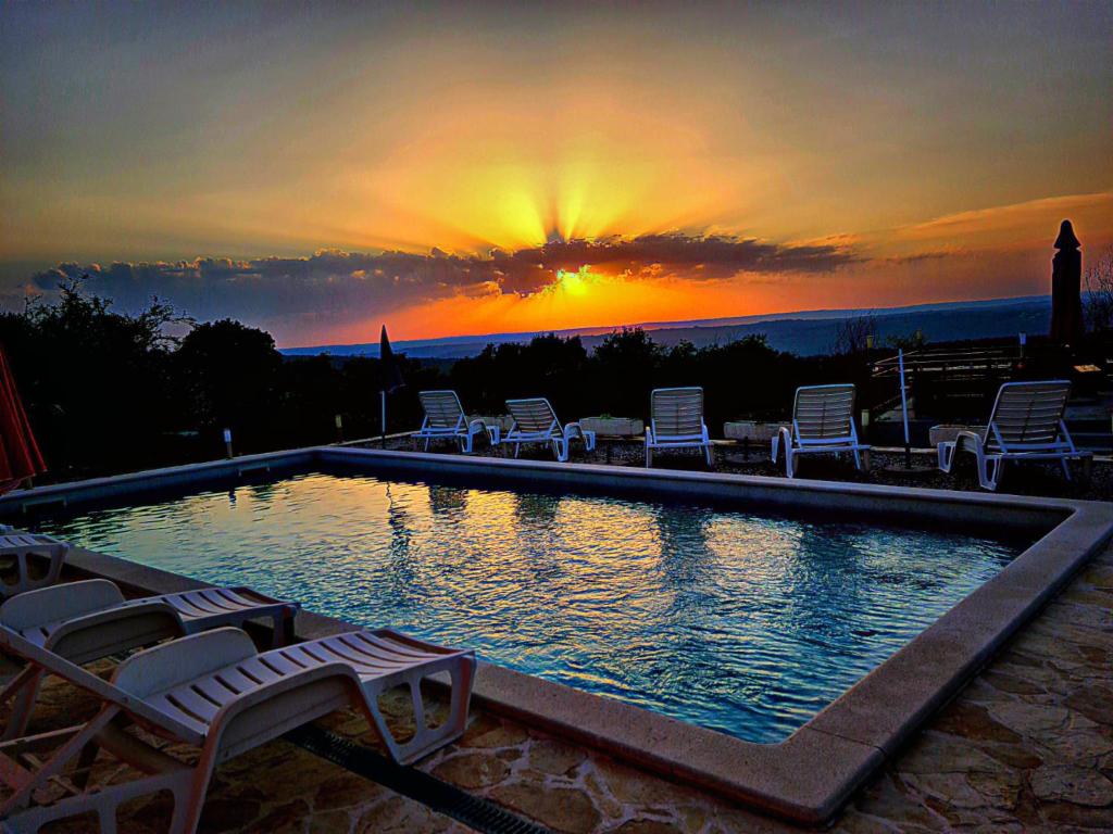 a pool with chairs and the sunset in the background at B&B Rogočana in Labin