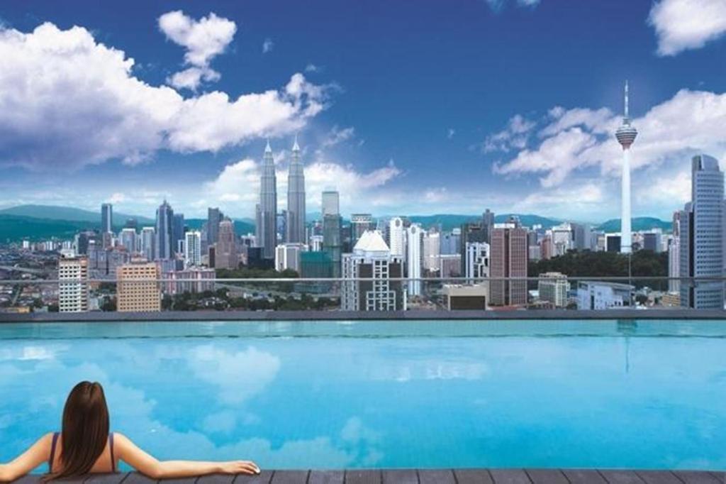 una mujer sentada en una piscina con vistas a una ciudad en Regalia Upper View Hotel, en Kuala Lumpur