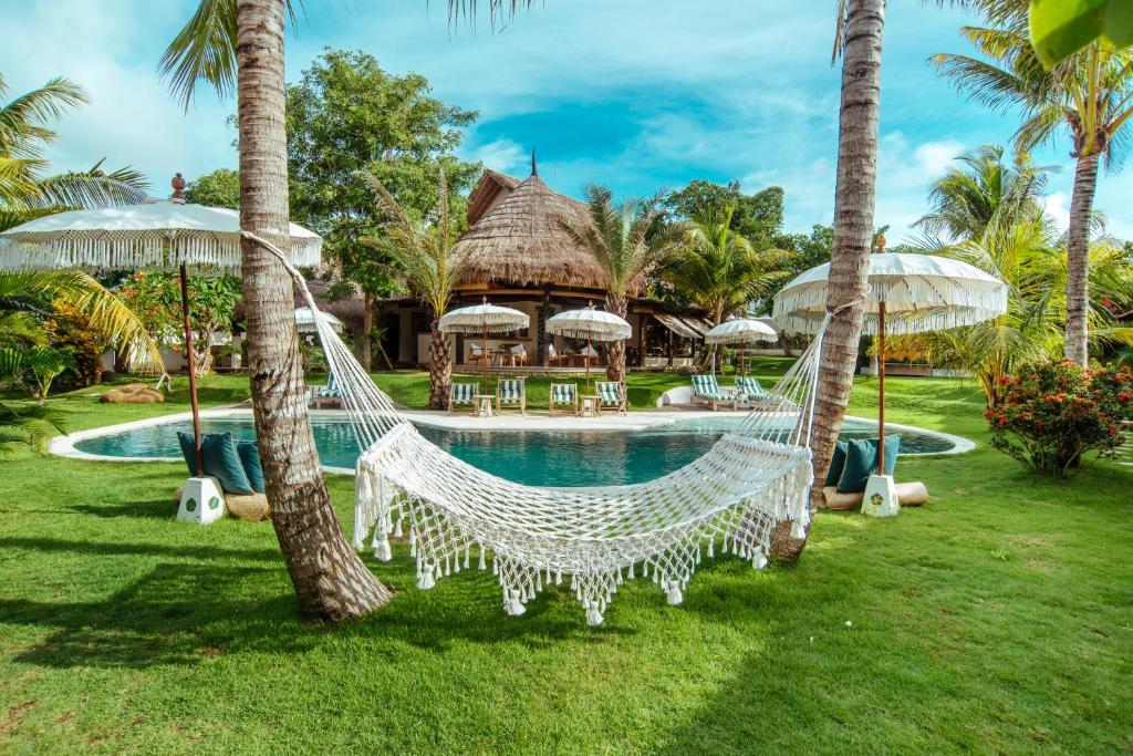 a hammock in front of a resort with a pool at Mule Malu Tropical Stay in Uluwatu