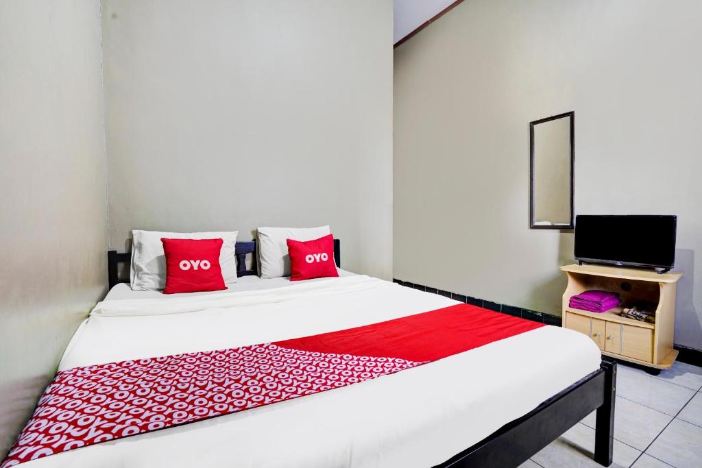 Schlafzimmer mit einem Bett mit roten Kissen und einem TV in der Unterkunft Super OYO 1I3676 Wisma Al-fahmi Syariah in Maniskaler