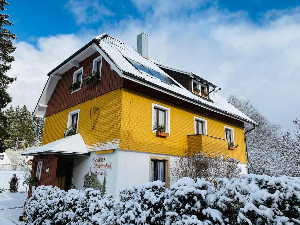 a yellow and brown house with snow on it at Gästehaus Sandvoss in Titisee-Neustadt