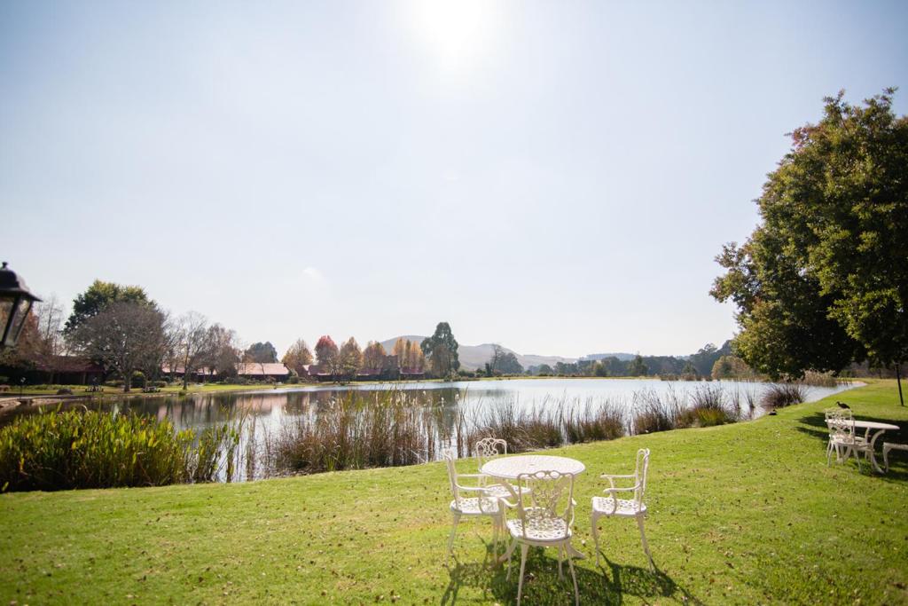 uma mesa e cadeiras na relva ao lado de um lago em Critchley Hackle em Dullstroom