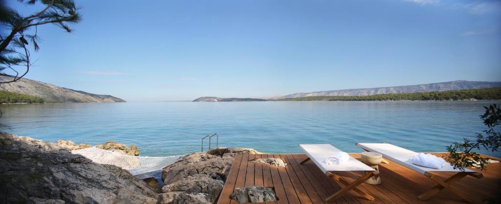 a wooden deck with two chairs on a body of water at Maslina Resort in Stari Grad