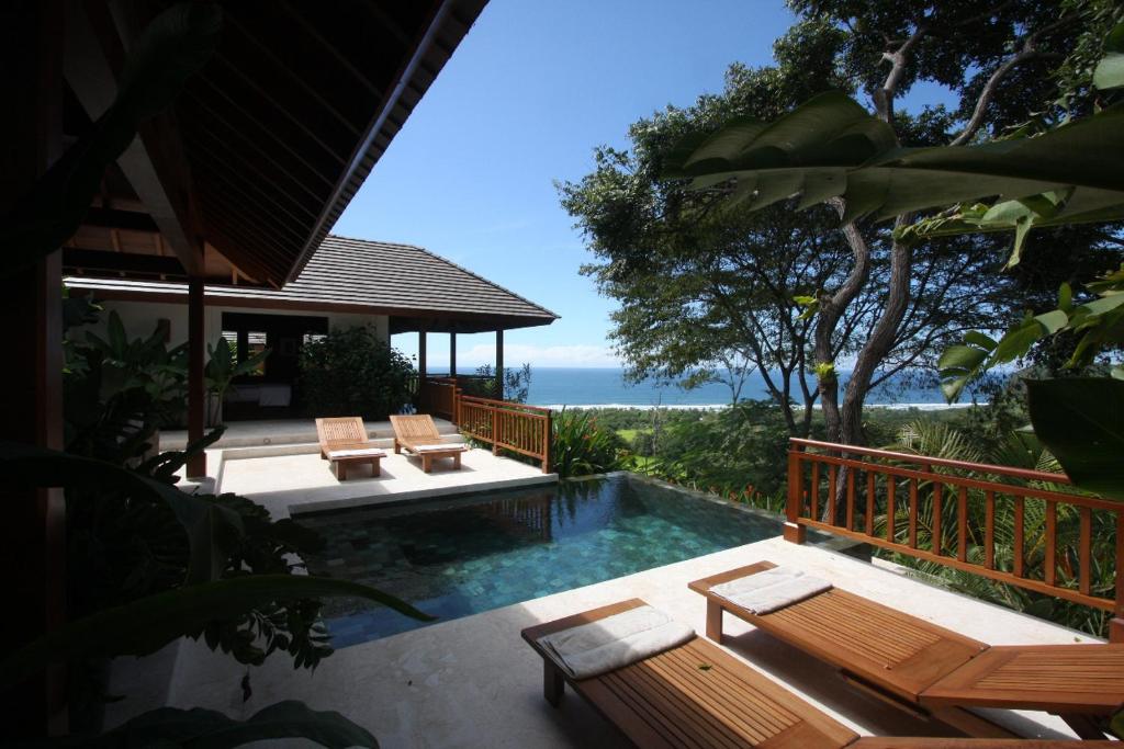 a swimming pool with benches and a house with the ocean at Canta La Rana in Bejuco