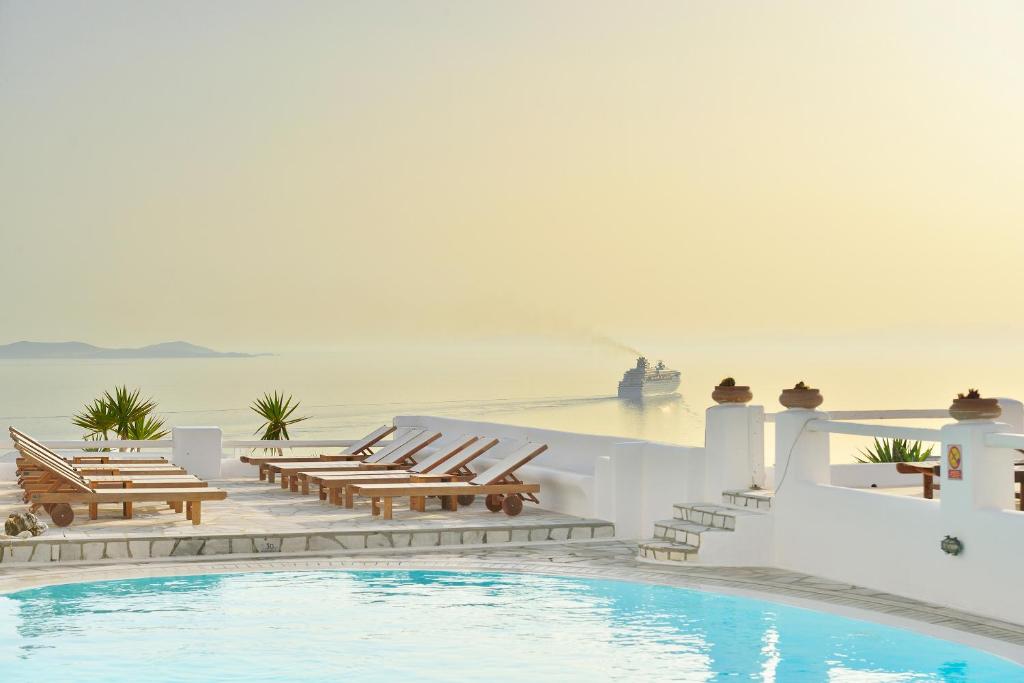 una piscina con mesas de madera y sillas junto al océano en Paolas Sunset, en Agios Stefanos