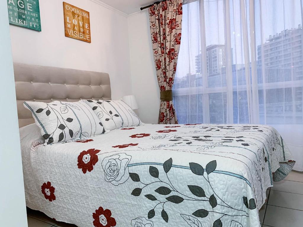 a bedroom with a bed with a flowered blanket and a window at Depto Metro Cal y Canto (Estudio) in Santiago