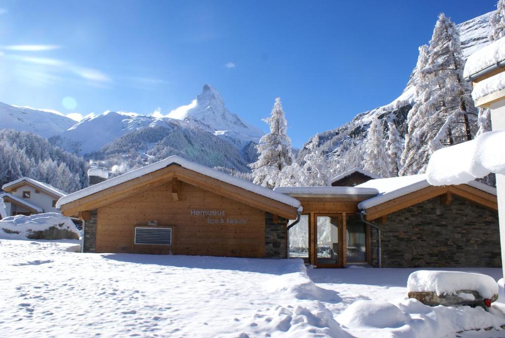 a building in the snow with mountains in the background at Hotel Hemizeus & Iremia Spa in Zermatt