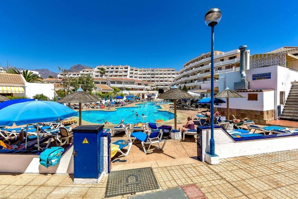 a swimming pool with people sitting in chairs and umbrellas at Garden City in Playa Fañabe