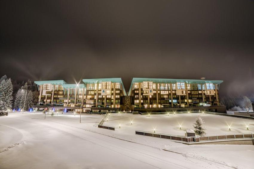 a building in the snow with a rink in front of it at Timber view apartment Silver Mountain Poiana Brasov in Poiana Brasov