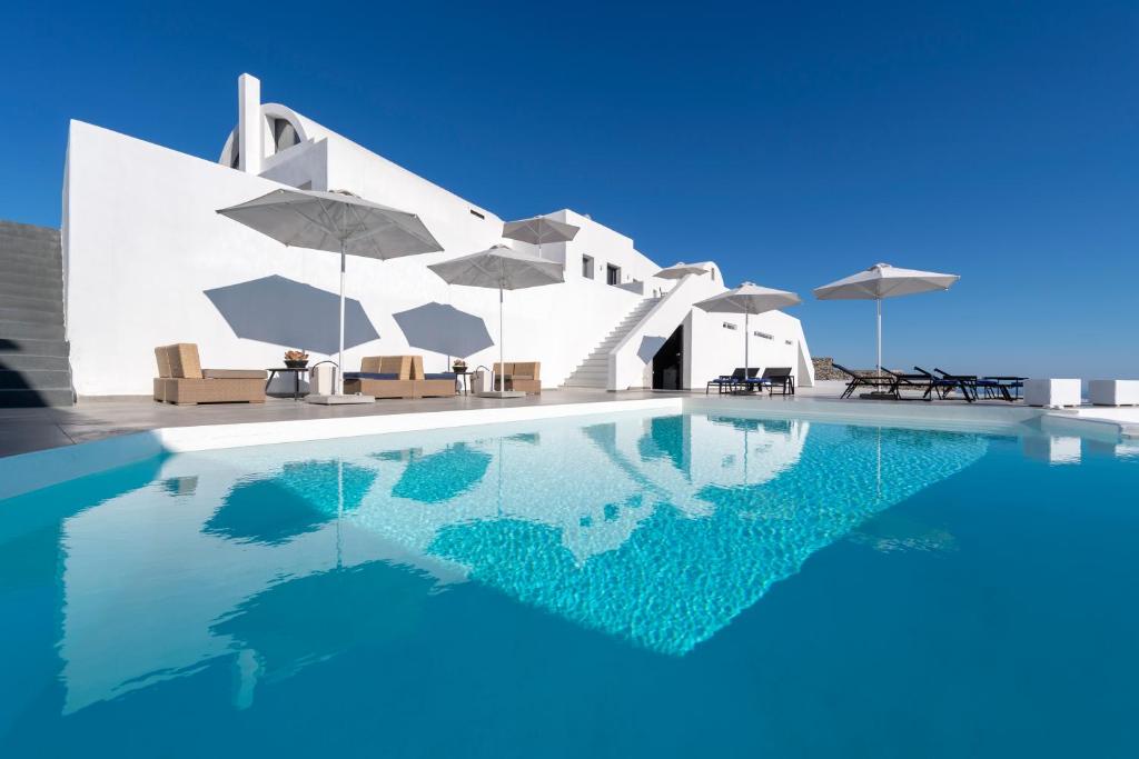 een zwembad voor een wit gebouw met parasols bij La Maltese Villas in Imerovígli