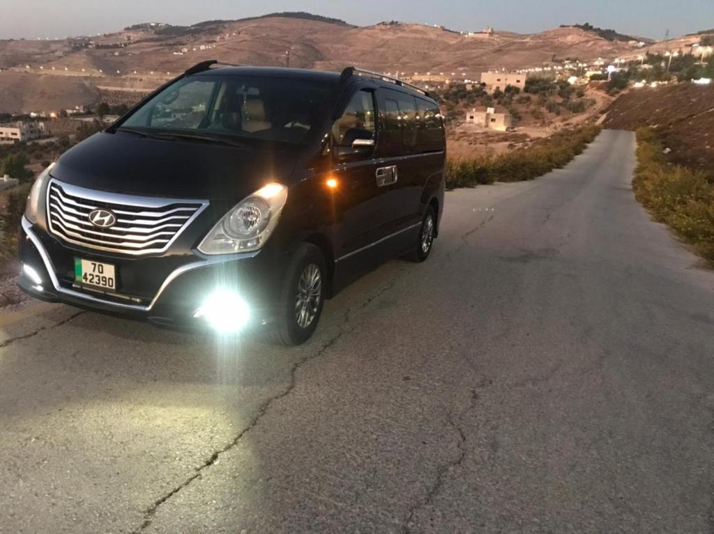 a black van is driving down a road at باص سياحي مع سائق و دليل سياحي متخصص in Al Qasţal