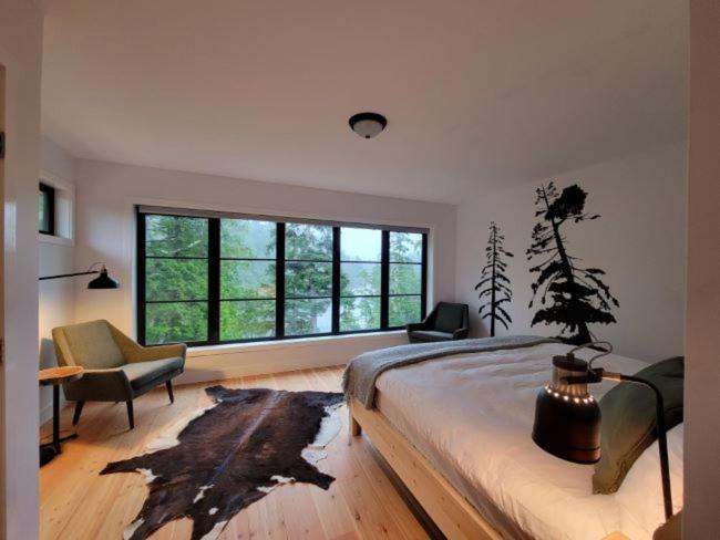 a bedroom with a bed and a chair and windows at Reef Point Cottages in Ucluelet