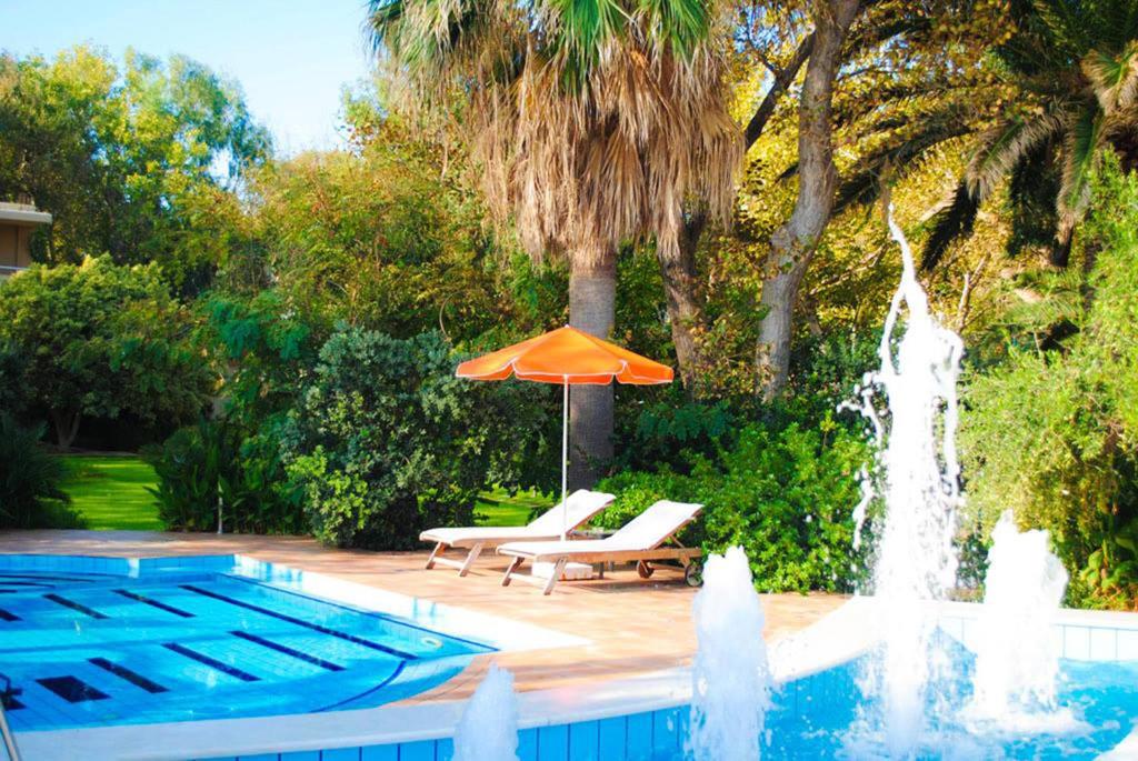 a pool with an umbrella and chairs and a fountain at Marita's Apartments in Agia Marina Nea Kydonias