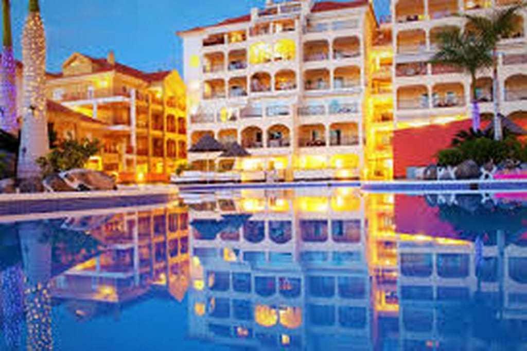 a view of a hotel with a reflection in the water at Dinastia B403 by Tenerife Rental and Sales in Los Cristianos