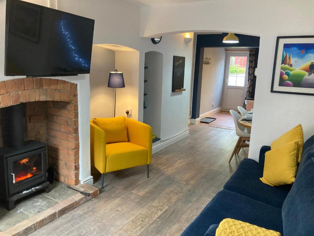 a living room with a fireplace and a yellow chair at Witcroft Cottage in Pershore