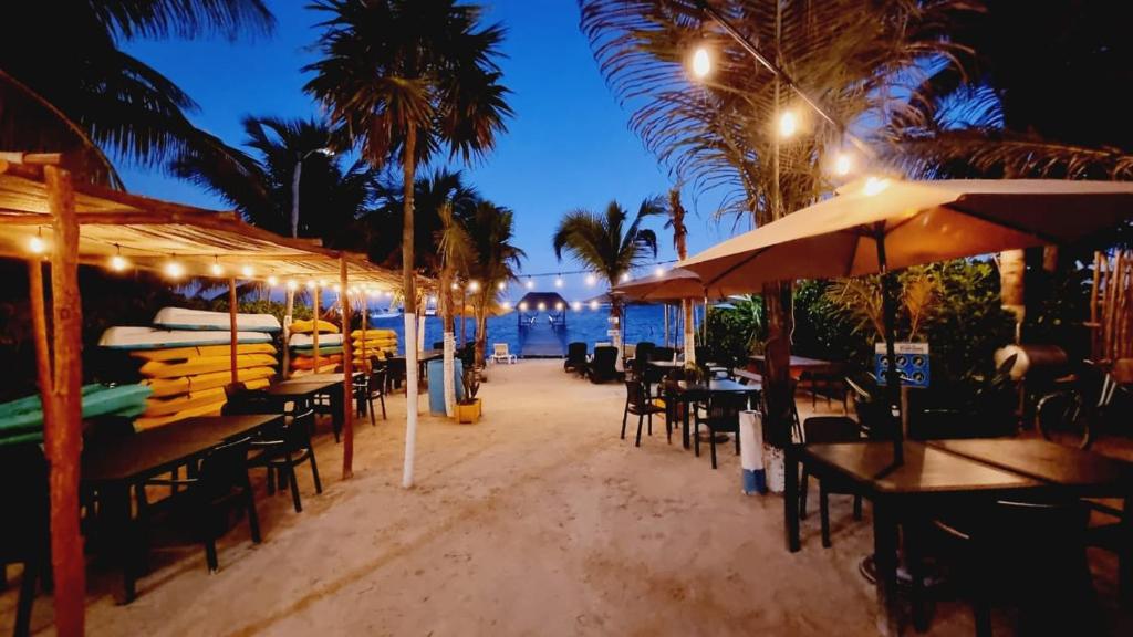 un restaurante con mesas y sombrillas en la playa por la noche en Hotel Machos Mahahual en Mahahual