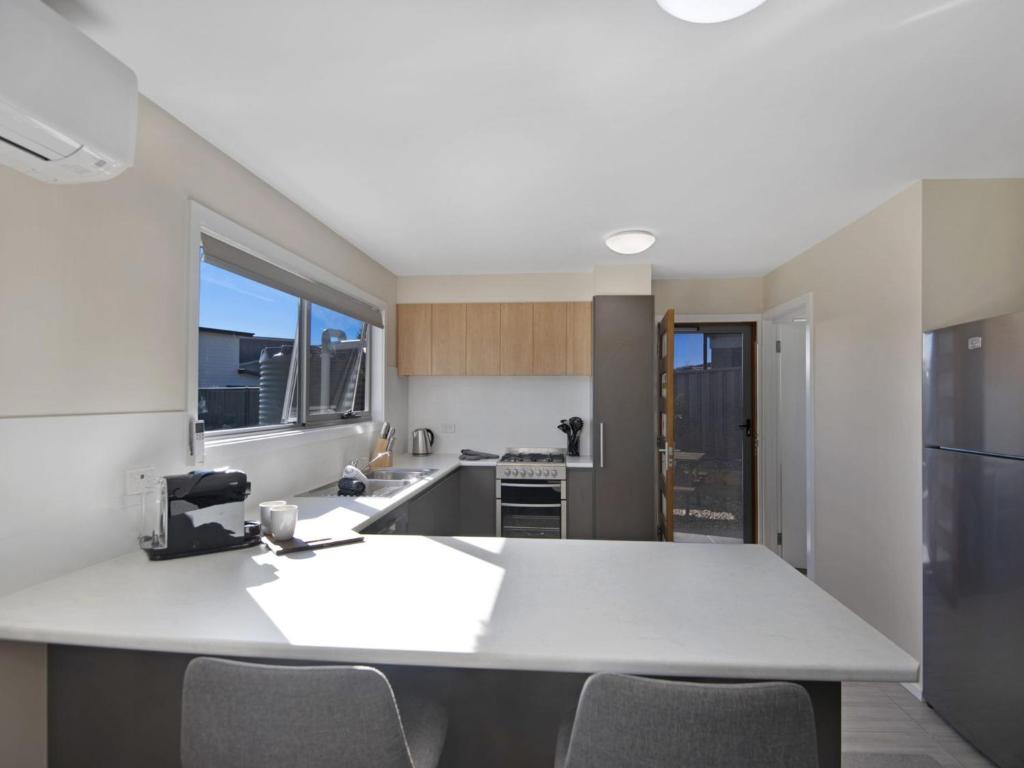 a kitchen with a white counter and chairs in it at T Bar on Twynam - Modern 2BR Apartment l WiFi l Netflix l BBQ l Smart TV l Air-Con in Jindabyne