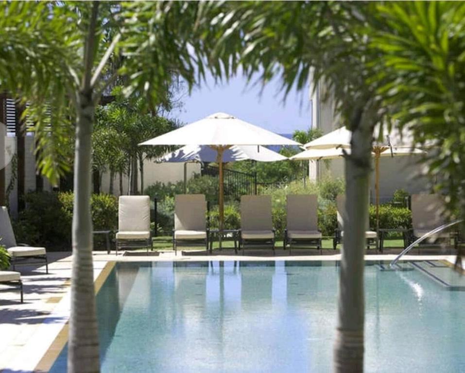 a pool with chairs and umbrellas and palm trees at Peppers Balé Luxury Beach Accommodation Kingscliff - privately let in Kingscliff