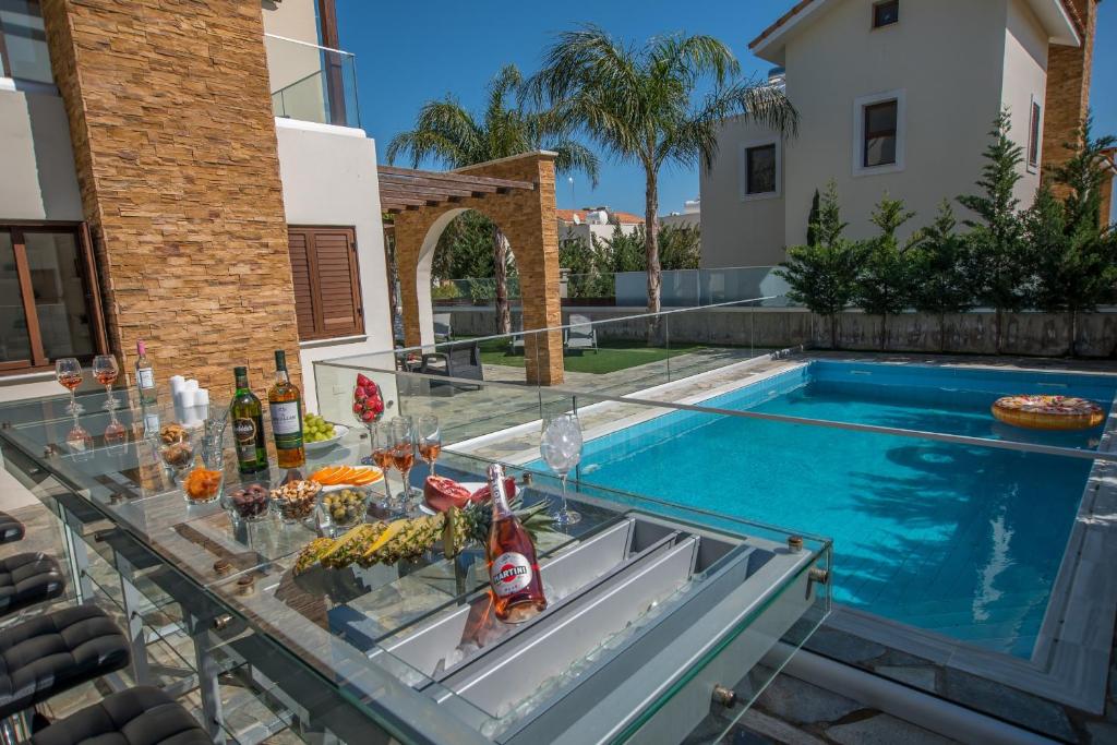 einen Tisch mit Speisen und Getränken auf einem Glastisch vor einem Pool in der Unterkunft Ayia Napa Ionion Seaside Villa in Ayia Napa