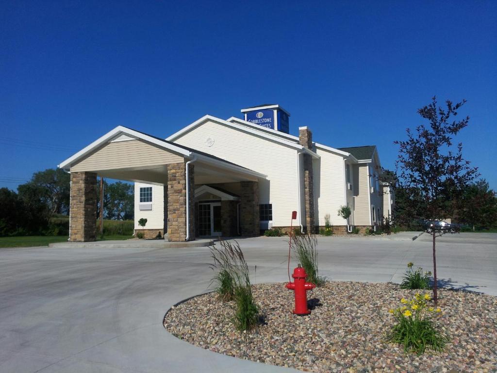 a building with a red fire hydrant in front of it at Cobblestone Inn & Suites - Hartington in Hartington