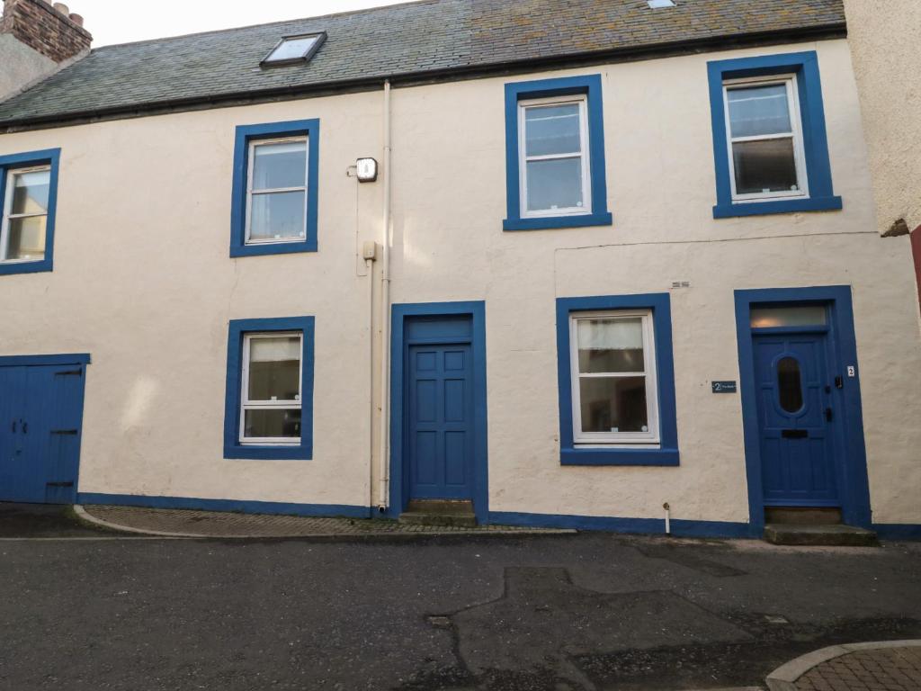 biały dom z niebieskimi drzwiami i oknami w obiekcie The Bield w mieście Eyemouth