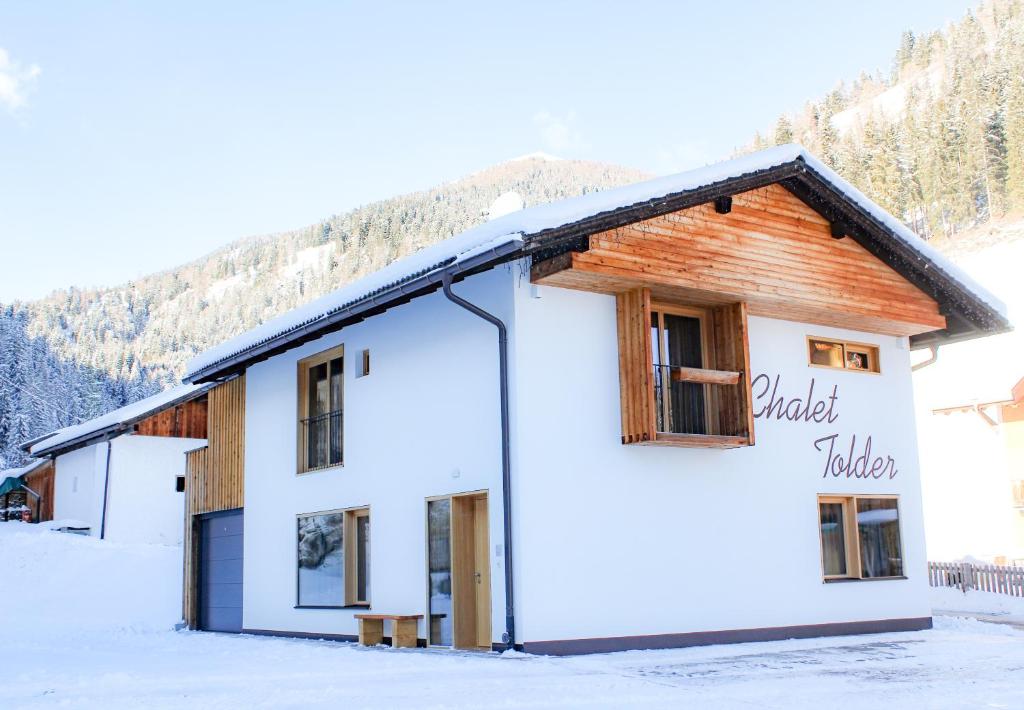 a white building with a wooden roof in the snow at Chalet Tolder in San Candido