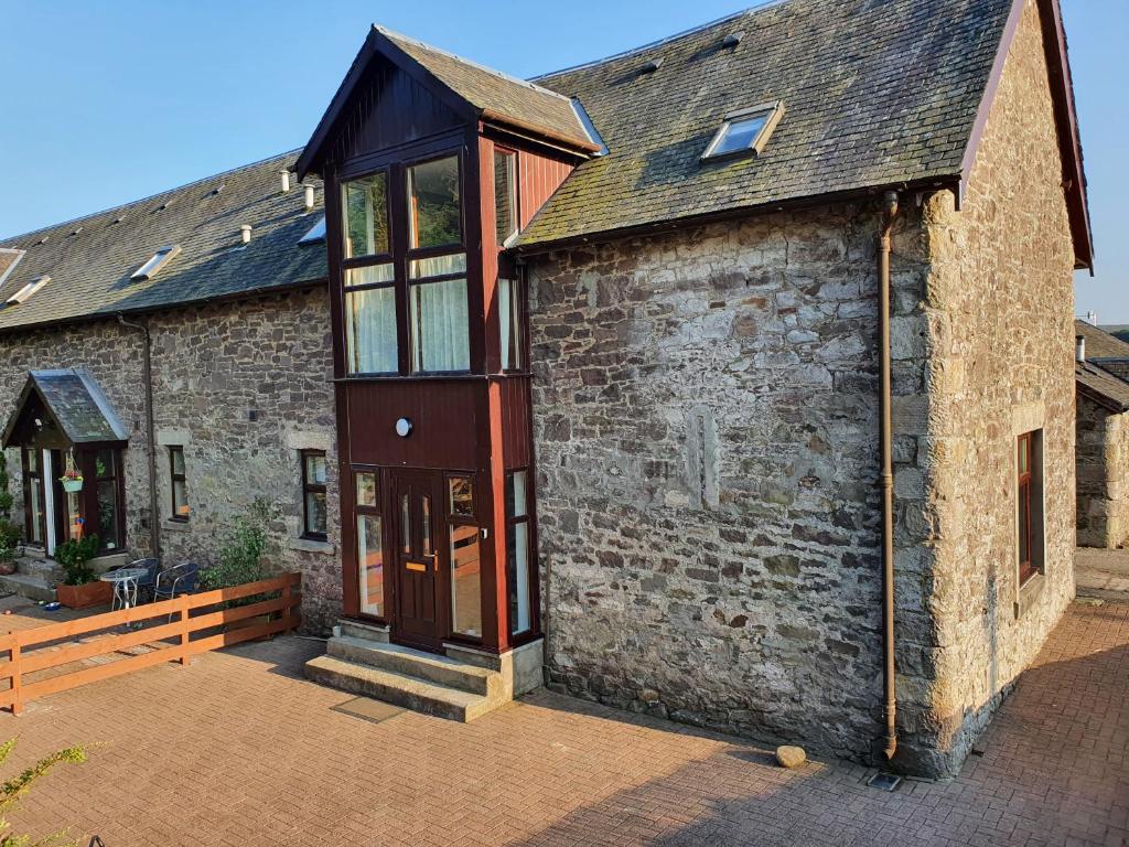 ein altes Backsteingebäude mit einer roten Tür und Fenstern in der Unterkunft The Granary at Tinto Retreats, Biggar is a gorgeous 3 bedroom Stone cottage in Wiston