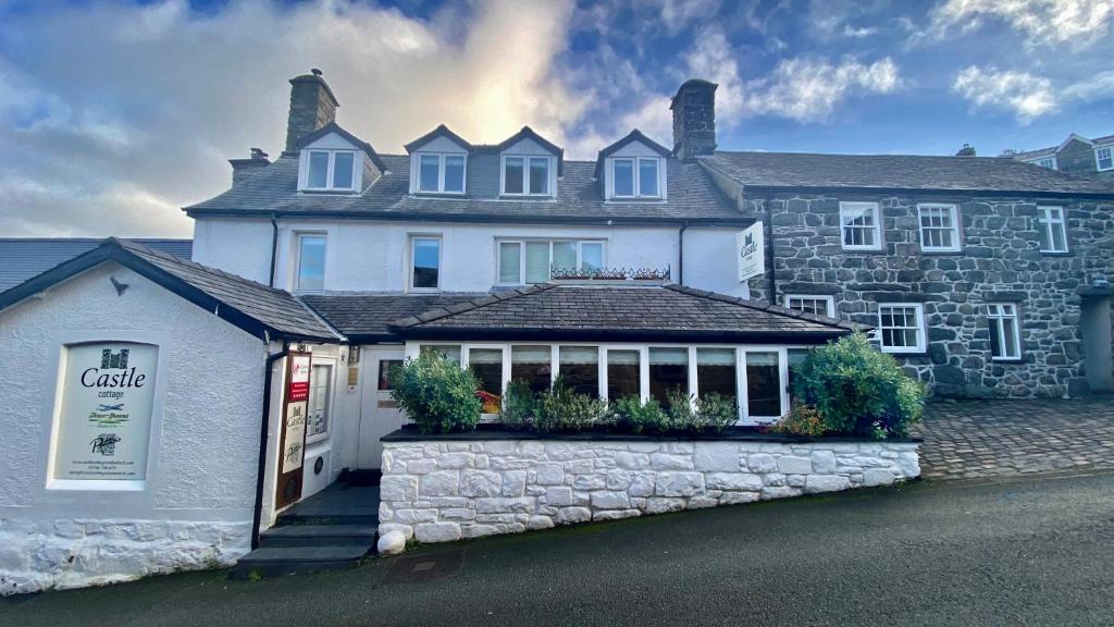 une grande maison blanche avec un bâtiment en pierre dans l'établissement Castle Cottage Inn, à Harlech