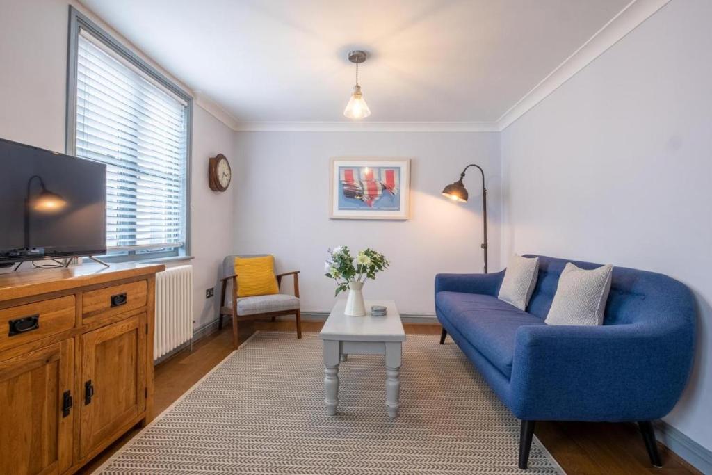 uma sala de estar com um sofá azul e uma televisão em Sailmaker's Cottage em Lymington