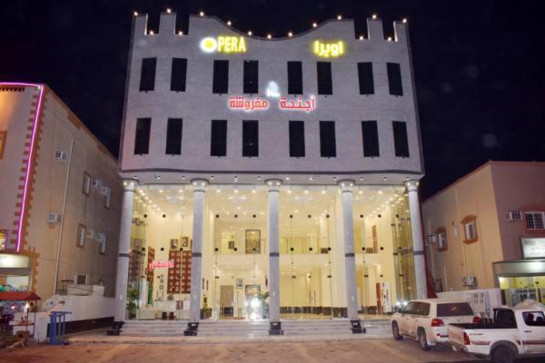 a large white building with lights in a parking lot at Opera Suites in Muhayil
