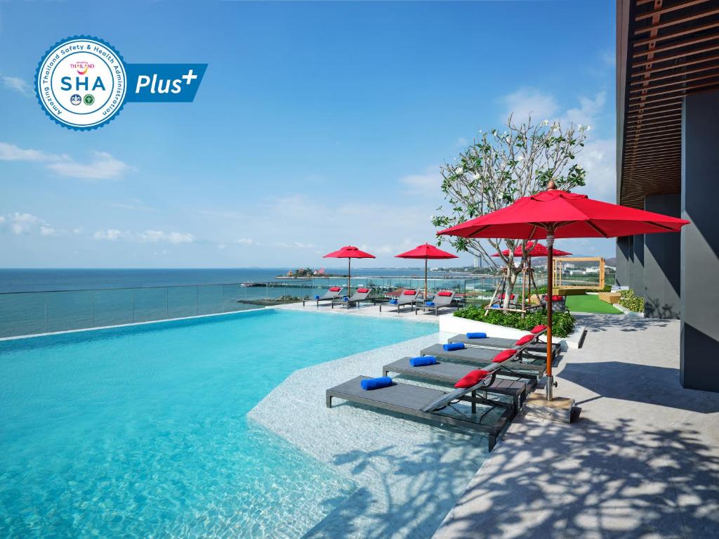 - une piscine avec chaises longues et parasols et l'océan dans l'établissement Novotel Marina Sriracha, à Si Racha