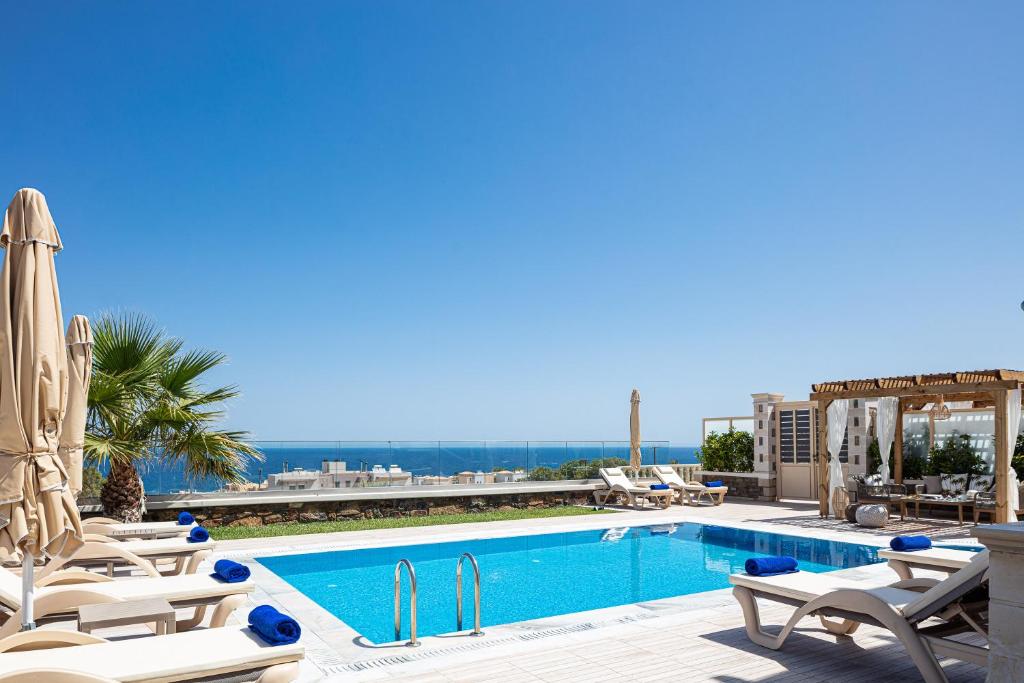 a swimming pool with chaise lounges and chairs next to a resort at Agapi Villas I & II, fairytale seaside retreats, By ThinkVilla in Panormos Rethymno