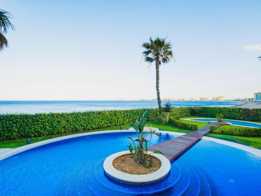 a swimming pool with a palm tree and the ocean at Apartment Punta Cormoran by Interhome in La Manga del Mar Menor