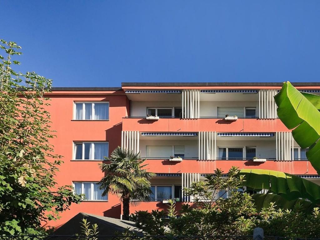 un bâtiment oranger avec des arbres devant lui dans l'établissement Apartment Double Room-3 by Interhome, à Ascona