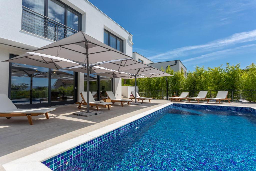 a swimming pool with chairs and umbrellas next to a house at Villa JoJo in Malinska